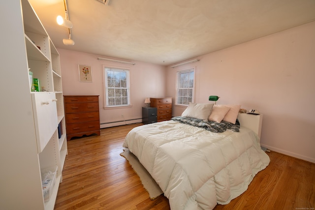 bedroom with light wood finished floors, baseboards, and a baseboard radiator