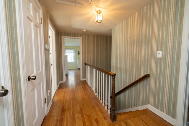 corridor featuring attic access, light wood-style flooring, baseboards, an upstairs landing, and wallpapered walls