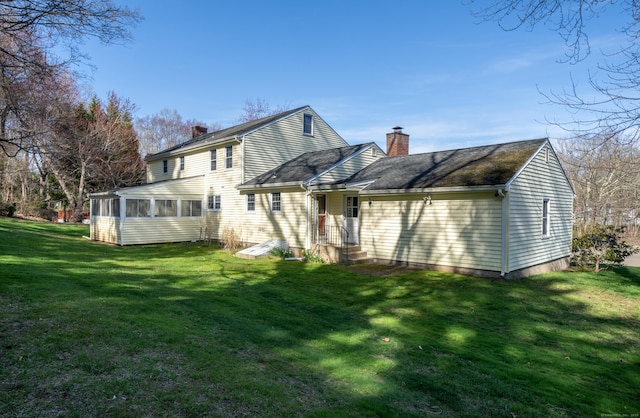 rear view of house with a chimney, a sunroom, and a lawn