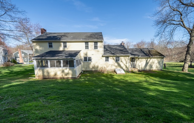 back of house featuring a yard, a sunroom, and a chimney