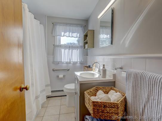 67 Stuart St, Newington, CT 06111 - full bathroom featuring a baseboard radiator, toilet, tile patterned flooring, a wainscoted wall, and vanity