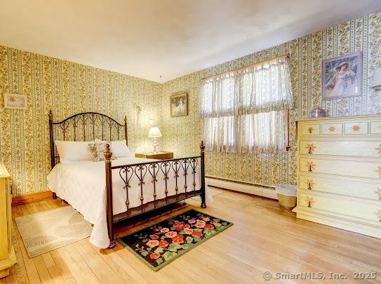 67 Stuart St, Newington, CT 06111 - bedroom featuring wallpapered walls, a baseboard radiator, wood finished floors, and baseboards