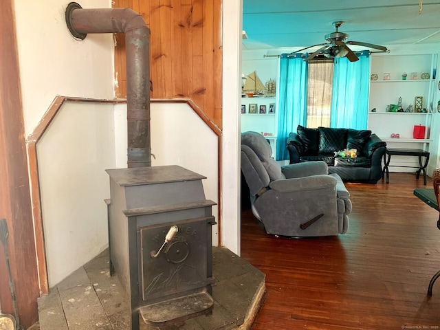 living room featuring a wood stove, wood finished floors, and ceiling fan