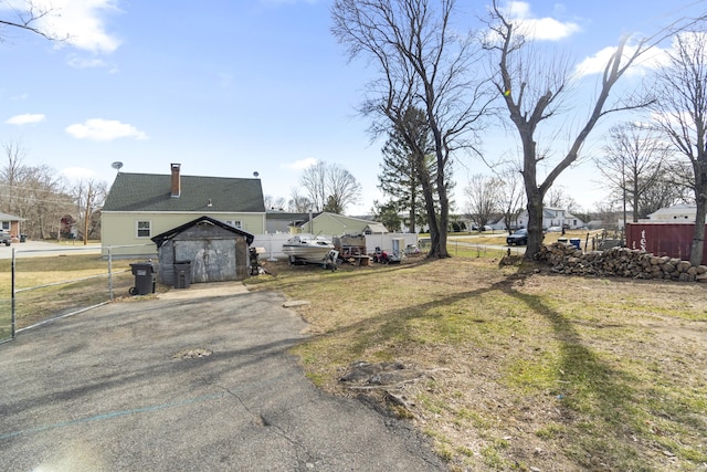exterior space featuring aphalt driveway, fence, an outbuilding, and a storage unit