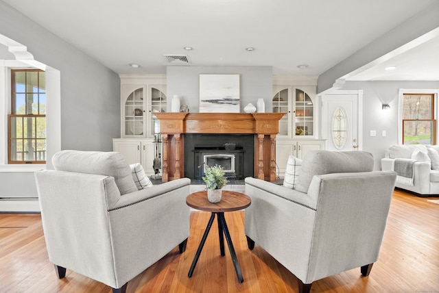 living area with baseboard heating, a fireplace, recessed lighting, light wood-type flooring, and visible vents