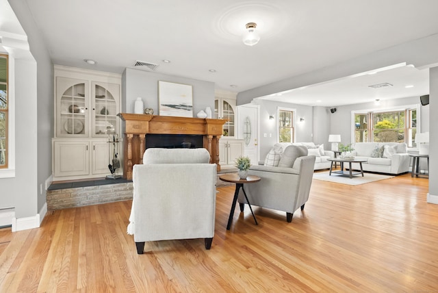 living room featuring visible vents, a fireplace, light wood-style floors, baseboards, and a baseboard radiator