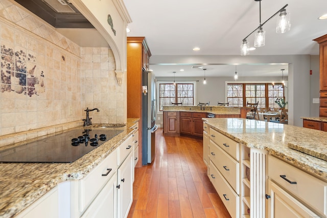 kitchen featuring freestanding refrigerator, recessed lighting, black electric stovetop, and light stone countertops