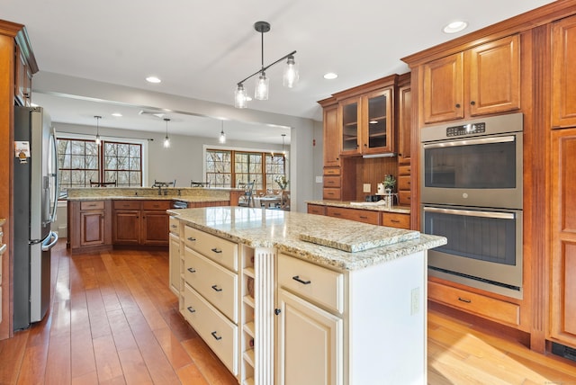 kitchen featuring glass insert cabinets, light wood finished floors, a kitchen island, and stainless steel appliances