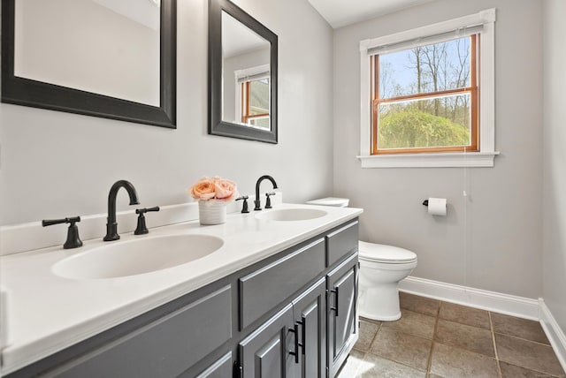 bathroom with a sink, baseboards, toilet, and double vanity