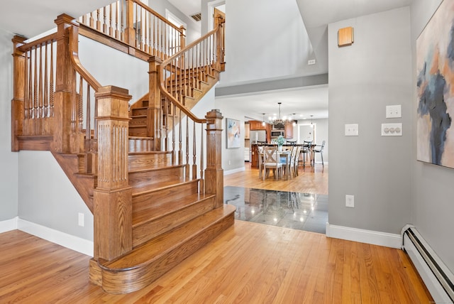 stairs with a notable chandelier, baseboards, a baseboard heating unit, and wood finished floors