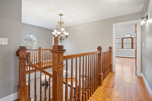 corridor with a notable chandelier, light wood-style floors, baseboards, an upstairs landing, and a baseboard radiator