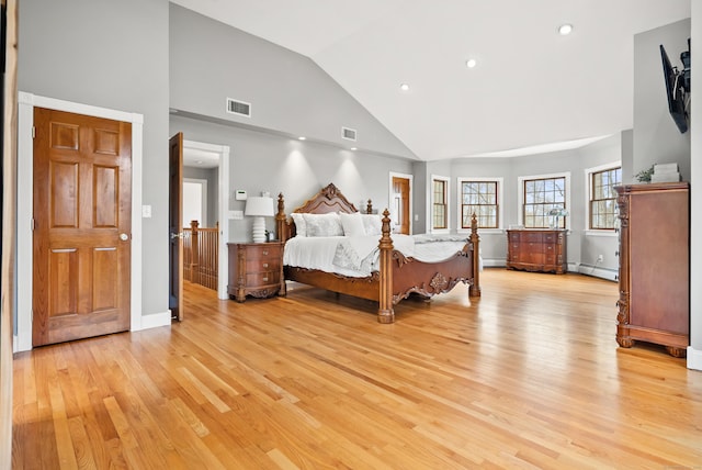 bedroom with visible vents, light wood finished floors, a baseboard heating unit, and high vaulted ceiling