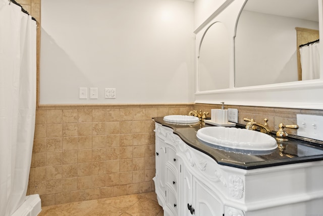 full bathroom with double vanity, tile walls, a wainscoted wall, tile patterned floors, and a sink