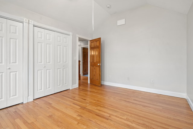 unfurnished bedroom featuring baseboards, two closets, light wood-type flooring, and high vaulted ceiling