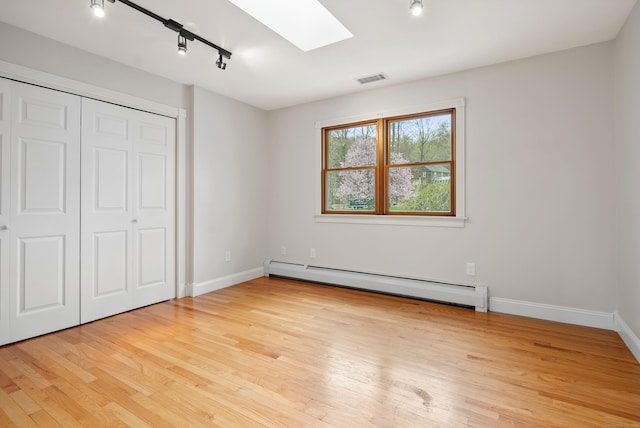 unfurnished bedroom with track lighting, baseboards, light wood-style floors, a baseboard heating unit, and a skylight