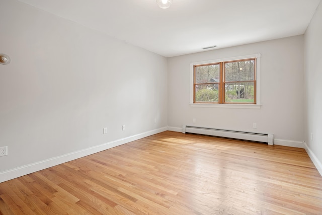 spare room featuring baseboards, a baseboard heating unit, light wood finished floors, and visible vents