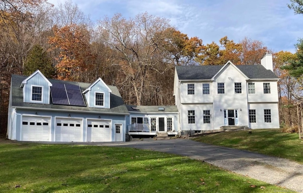 view of front facade with roof mounted solar panels, driveway, a garage, and a front yard
