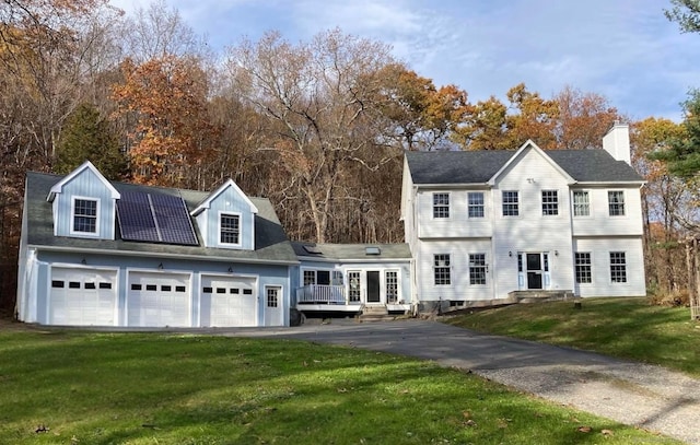 view of front facade with roof mounted solar panels, driveway, a garage, and a front yard