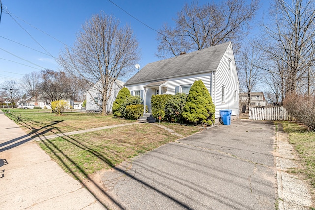 view of front of property with roof with shingles, a chimney, aphalt driveway, a front yard, and fence