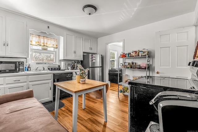 kitchen with freestanding refrigerator, light wood-type flooring, white cabinets, black dishwasher, and light countertops
