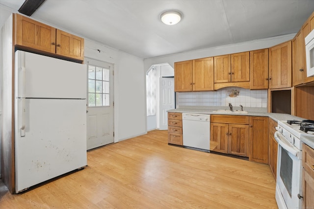 kitchen featuring white appliances, tasteful backsplash, light wood finished floors, light countertops, and a sink