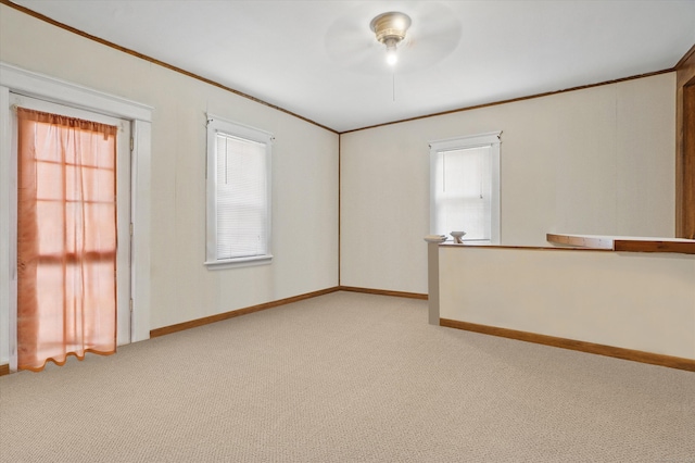 empty room with light carpet, crown molding, plenty of natural light, and baseboards