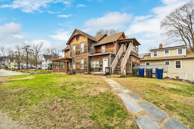 rear view of house featuring covered porch, stairs, and a lawn