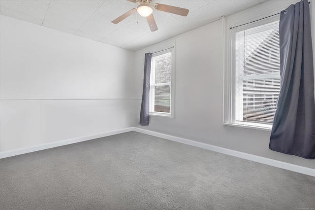 carpeted empty room with a wealth of natural light, ceiling fan, a drop ceiling, and baseboards