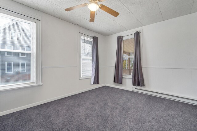 carpeted empty room featuring baseboard heating, ceiling fan, and a wealth of natural light