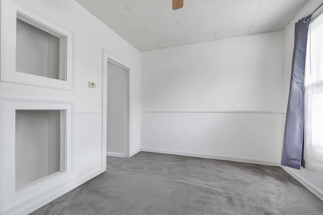 unfurnished living room featuring a drop ceiling, a ceiling fan, carpet flooring, and baseboards