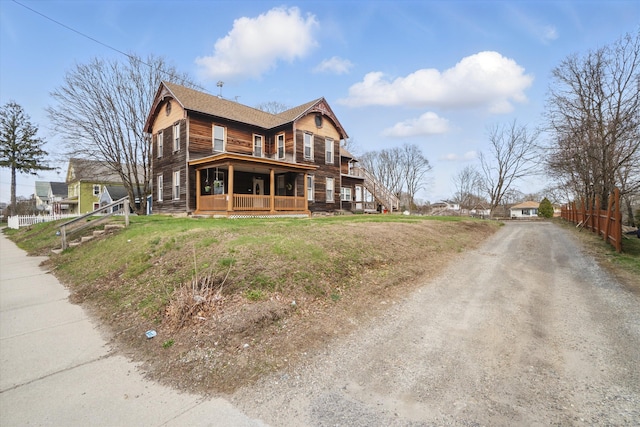 view of front facade with covered porch, fence, dirt driveway, and a shingled roof