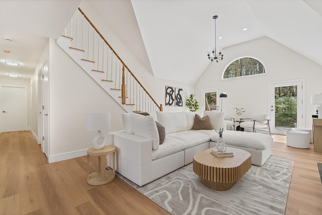 living room with light wood-style flooring, baseboards, an inviting chandelier, high vaulted ceiling, and stairs