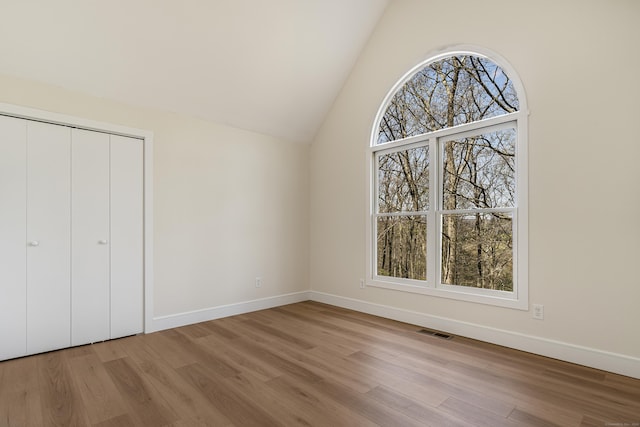 unfurnished bedroom featuring a closet, wood finished floors, visible vents, baseboards, and lofted ceiling