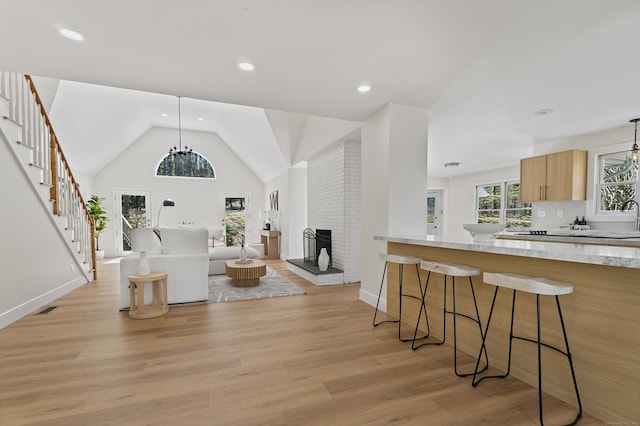living room featuring stairway, light wood-style floors, a brick fireplace, baseboards, and visible vents