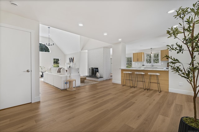 living room with lofted ceiling, light wood-style floors, a notable chandelier, and a brick fireplace
