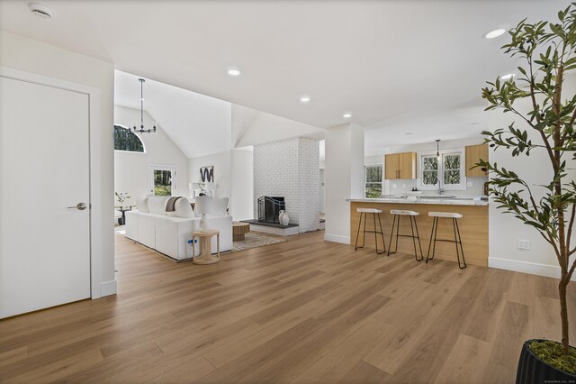 living area featuring a fireplace, a chandelier, light wood-style flooring, and vaulted ceiling
