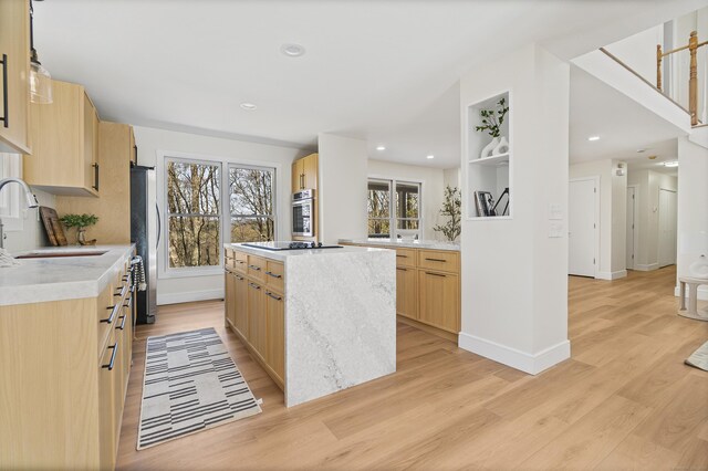 kitchen featuring light brown cabinetry, stainless steel appliances, light wood finished floors, a sink, and a center island