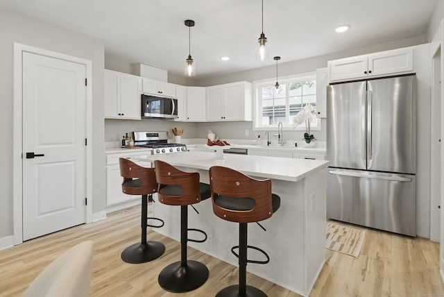 kitchen with light countertops, a kitchen island, stainless steel appliances, light wood finished floors, and a sink