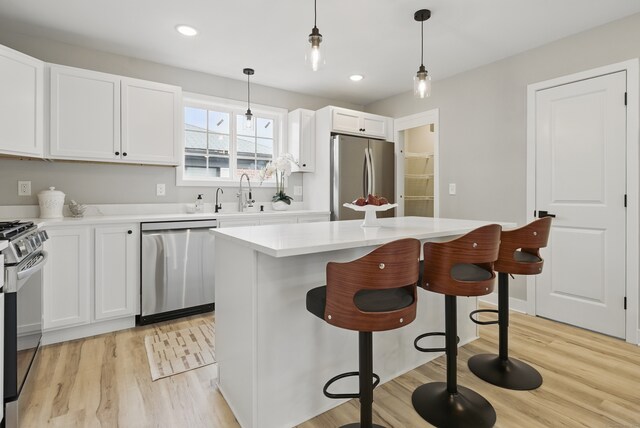 kitchen with stainless steel appliances, light wood-type flooring, white cabinetry, and hanging light fixtures