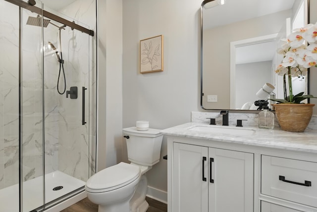 bathroom featuring baseboards, toilet, vanity, wood finished floors, and a marble finish shower