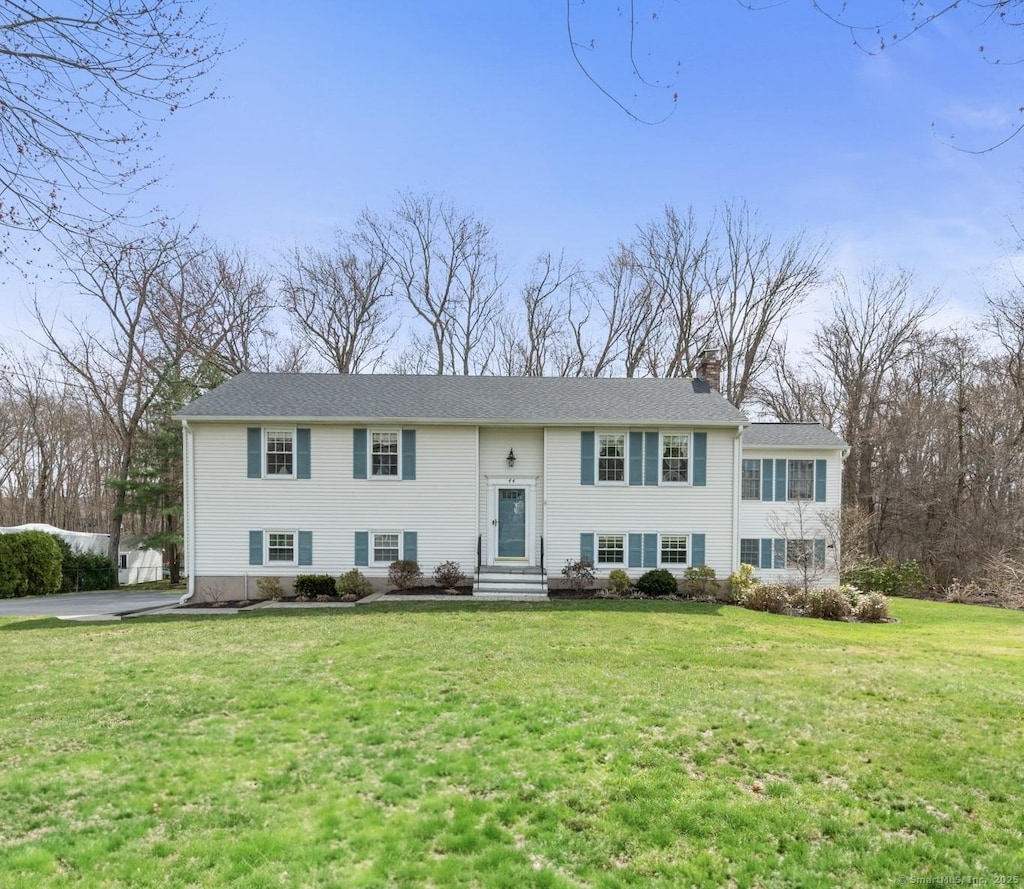 raised ranch featuring entry steps, a front lawn, and a chimney