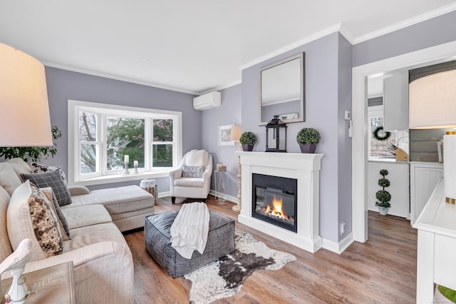 living area featuring a glass covered fireplace, baseboards, wood finished floors, a wall mounted AC, and ornamental molding