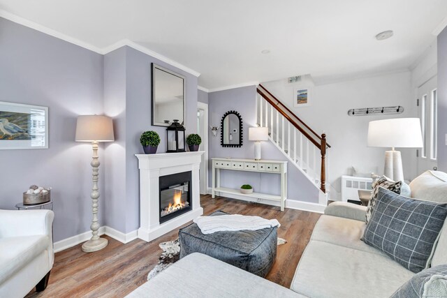 living area with stairway, crown molding, a glass covered fireplace, and wood finished floors