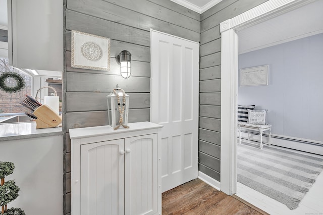 room details featuring a baseboard heating unit, wooden walls, wood finished floors, and ornamental molding