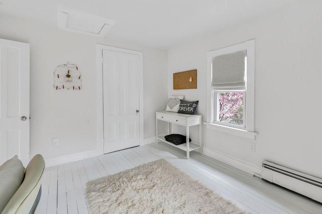 interior space with a baseboard heating unit, baseboards, wood finished floors, and attic access