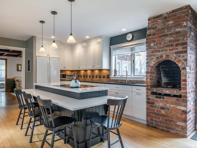 kitchen with freestanding refrigerator, light wood-style flooring, tasteful backsplash, a sink, and black electric cooktop