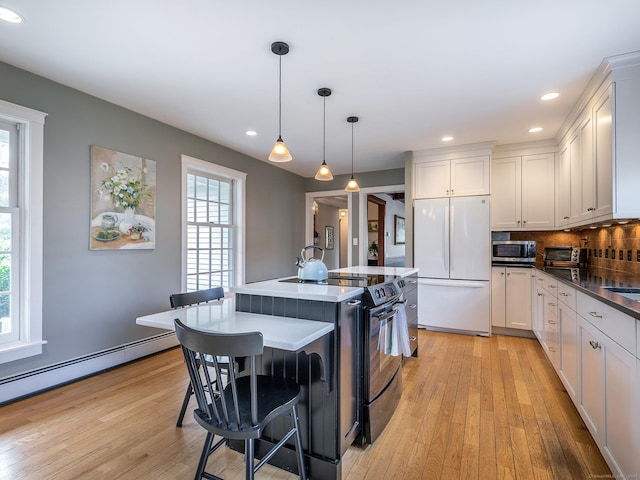 kitchen featuring stainless steel microwave, white fridge, light wood-style flooring, electric range, and a center island with sink
