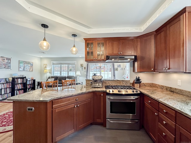 kitchen with stainless steel range with gas cooktop, a peninsula, a tray ceiling, decorative light fixtures, and under cabinet range hood