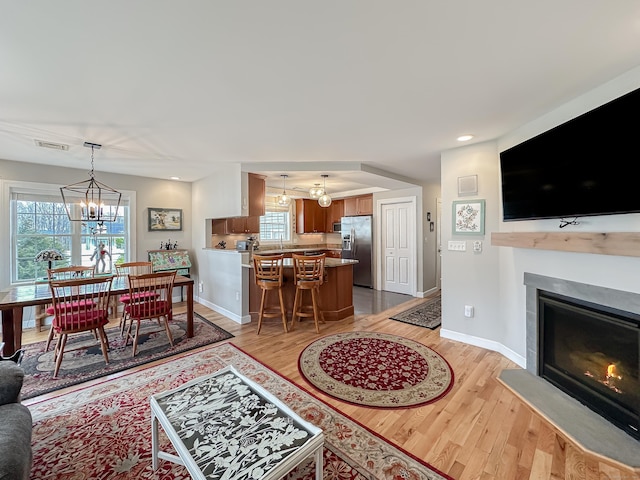 living area with a glass covered fireplace, light wood-style flooring, visible vents, and an inviting chandelier