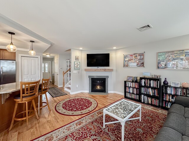 living room featuring a fireplace with flush hearth, recessed lighting, light wood finished floors, visible vents, and baseboards